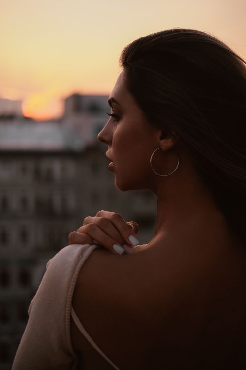 Free Profile of a woman gazing at the sunset from a cityscape view, exuding elegance and calmness. Stock Photo