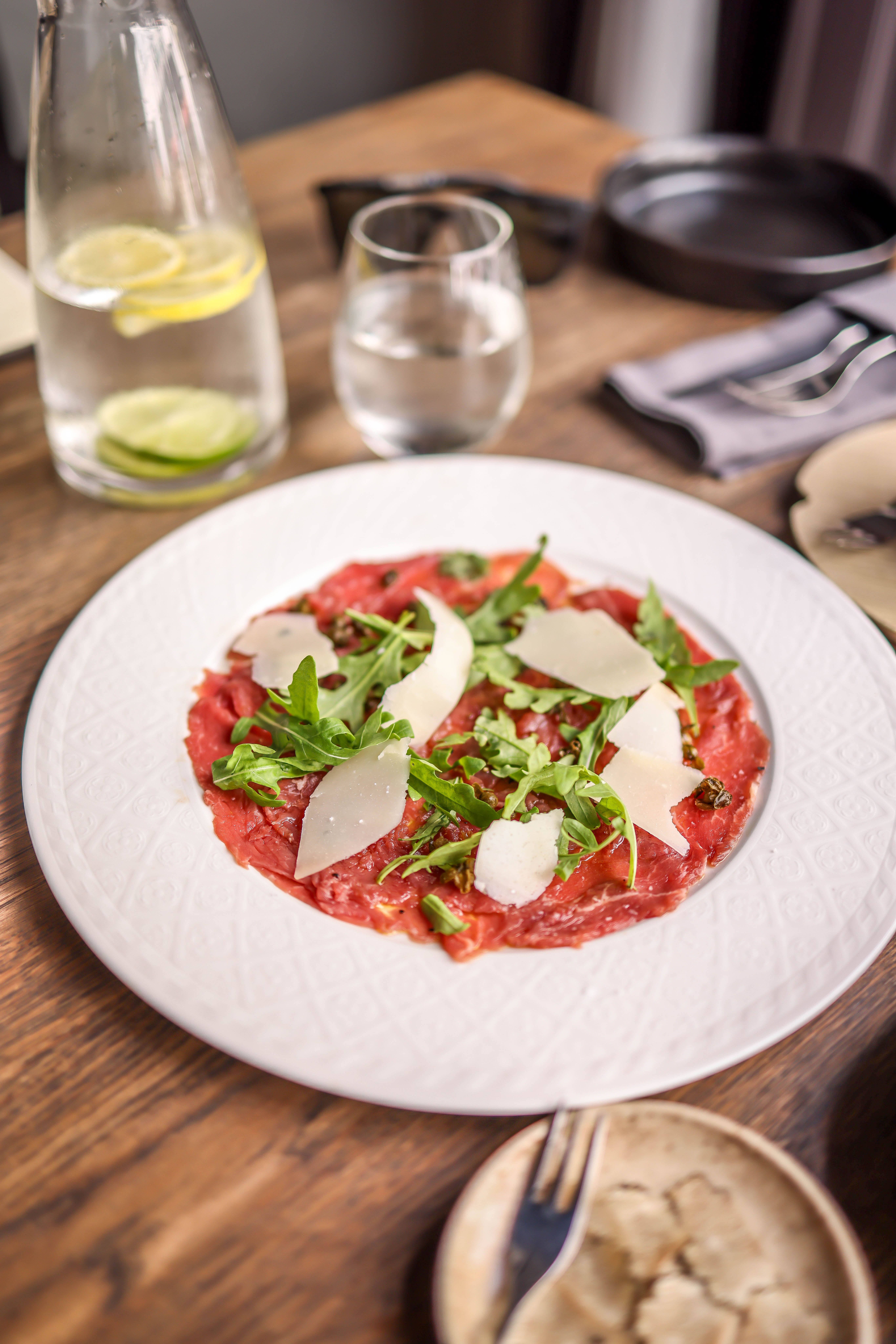 Plated dish of sliced meat with fresh vegetables showing classic carpaccio-style presentation