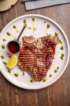Delicious grilled T-bone steak served with sauce and lemon on a wooden table.