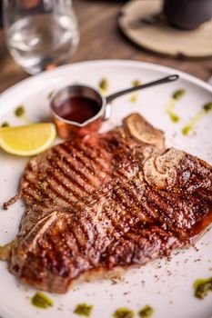 Delicious grilled beef steak served with sauce and a wedge of lemon on a white plate.