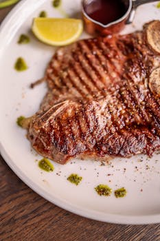 Delicious grilled beef steak served with lemon wedge and dipping sauce on a plate.
