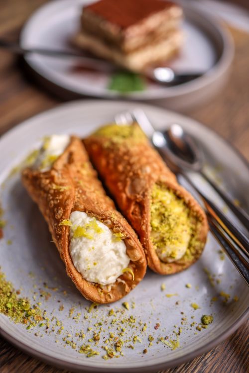 Free Close-up of traditional Italian cannoli filled with cream and topped with pistachios on a ceramic plate. Stock Photo