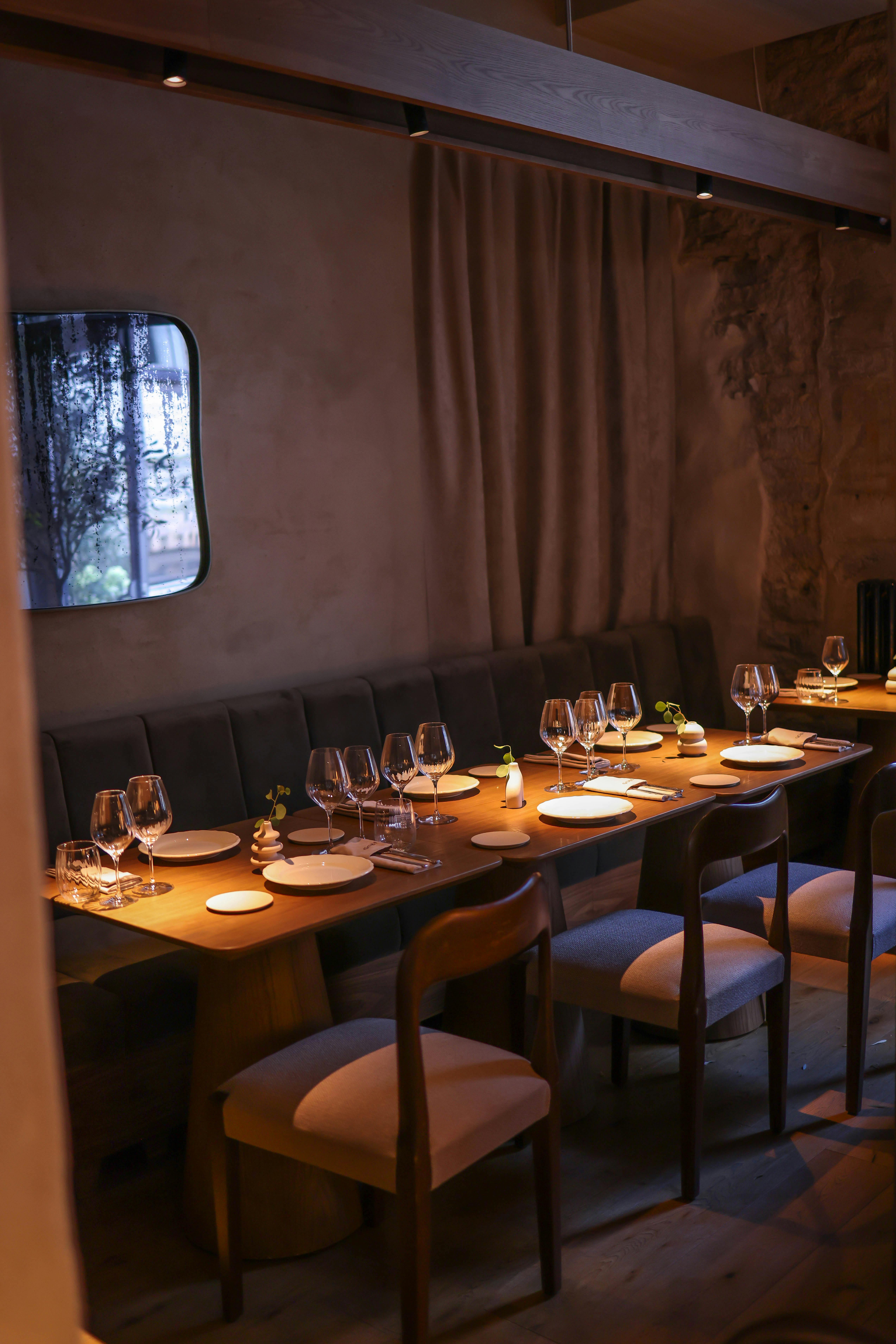 A long restaurant table set under warm pendant lighting with candles and polished glassware
