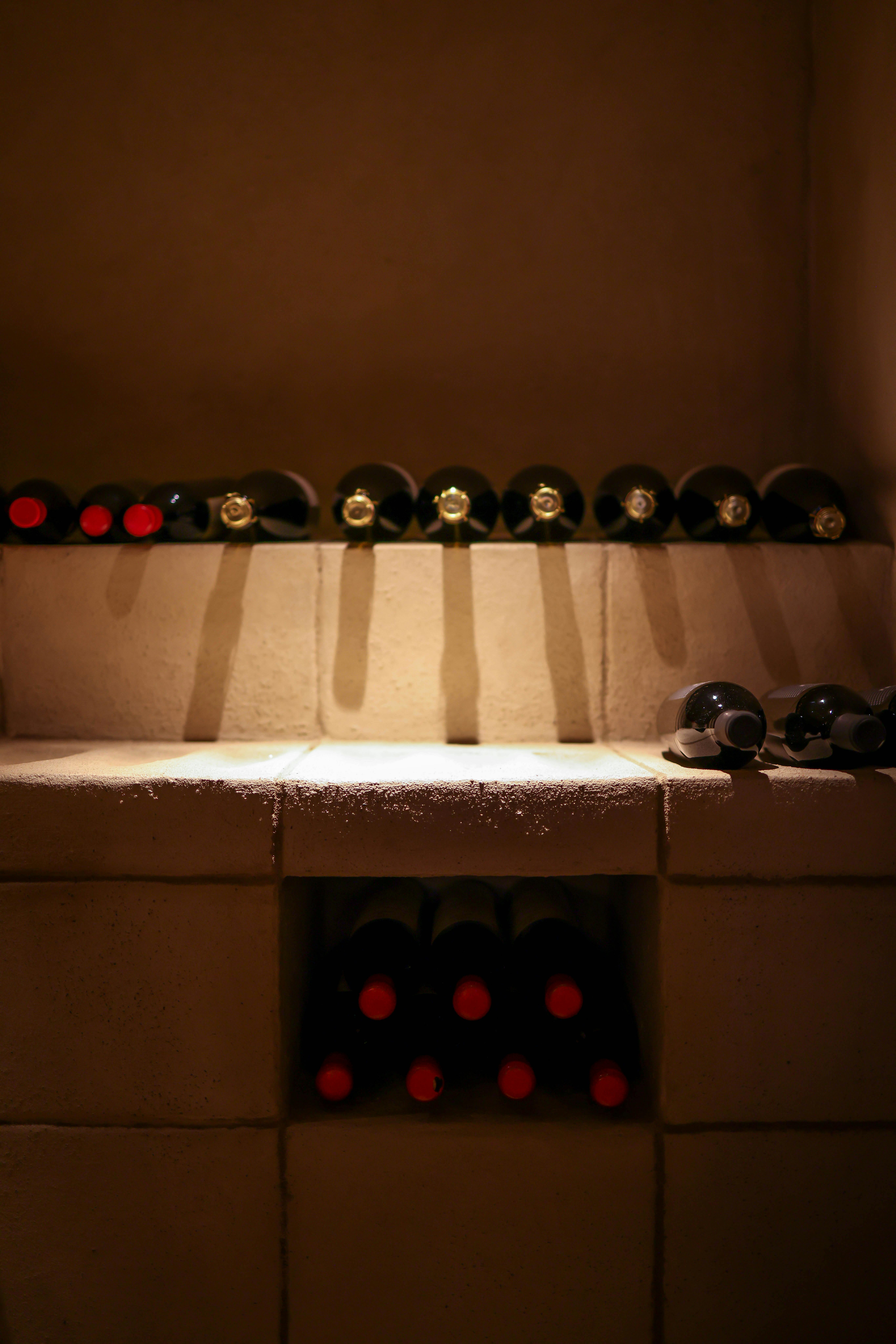 A dim-lit wine cellar featuring rows of vintage bottles stored on dusty wooden shelves.