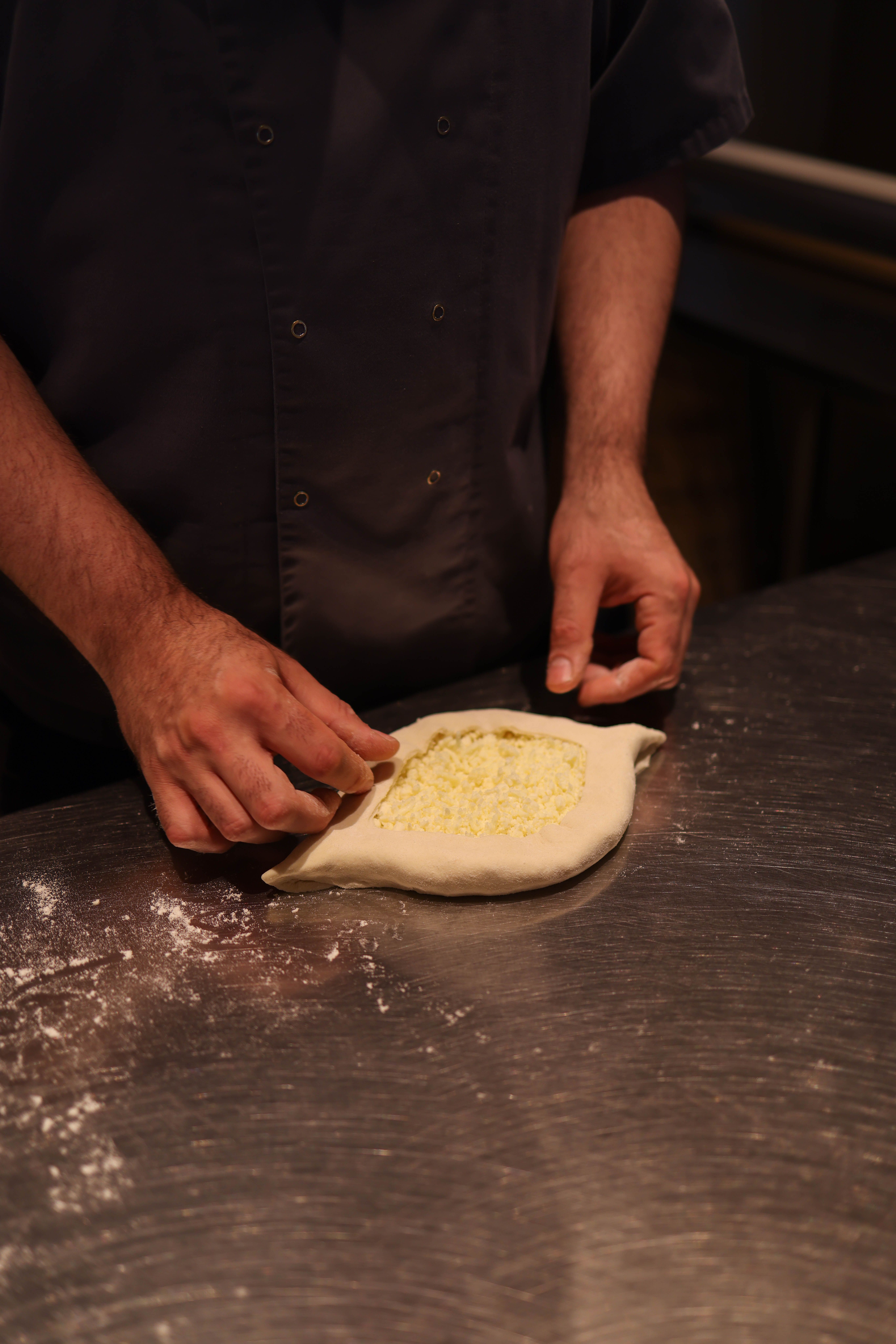 Chef shaping dough with cheese filling on a metal surface.