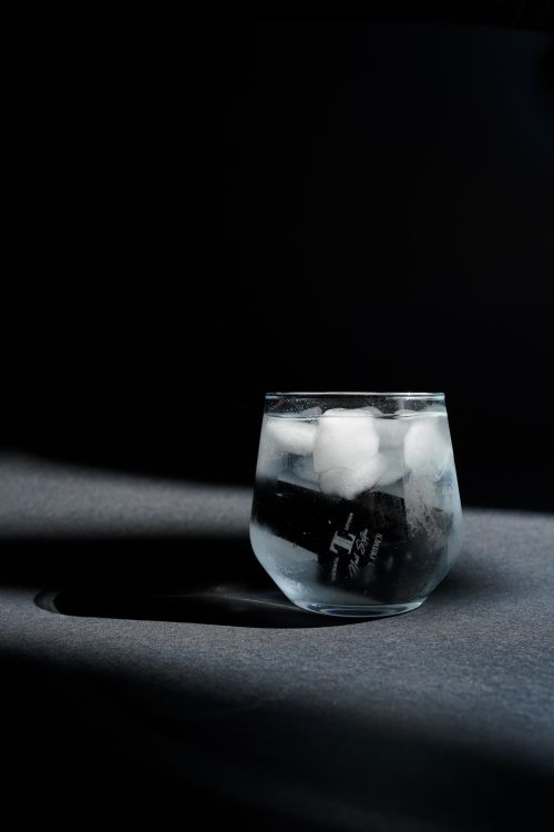 Free A glass of chilled beverage with ice cubes casting a shadow, creating a moody still life scene. Stock Photo