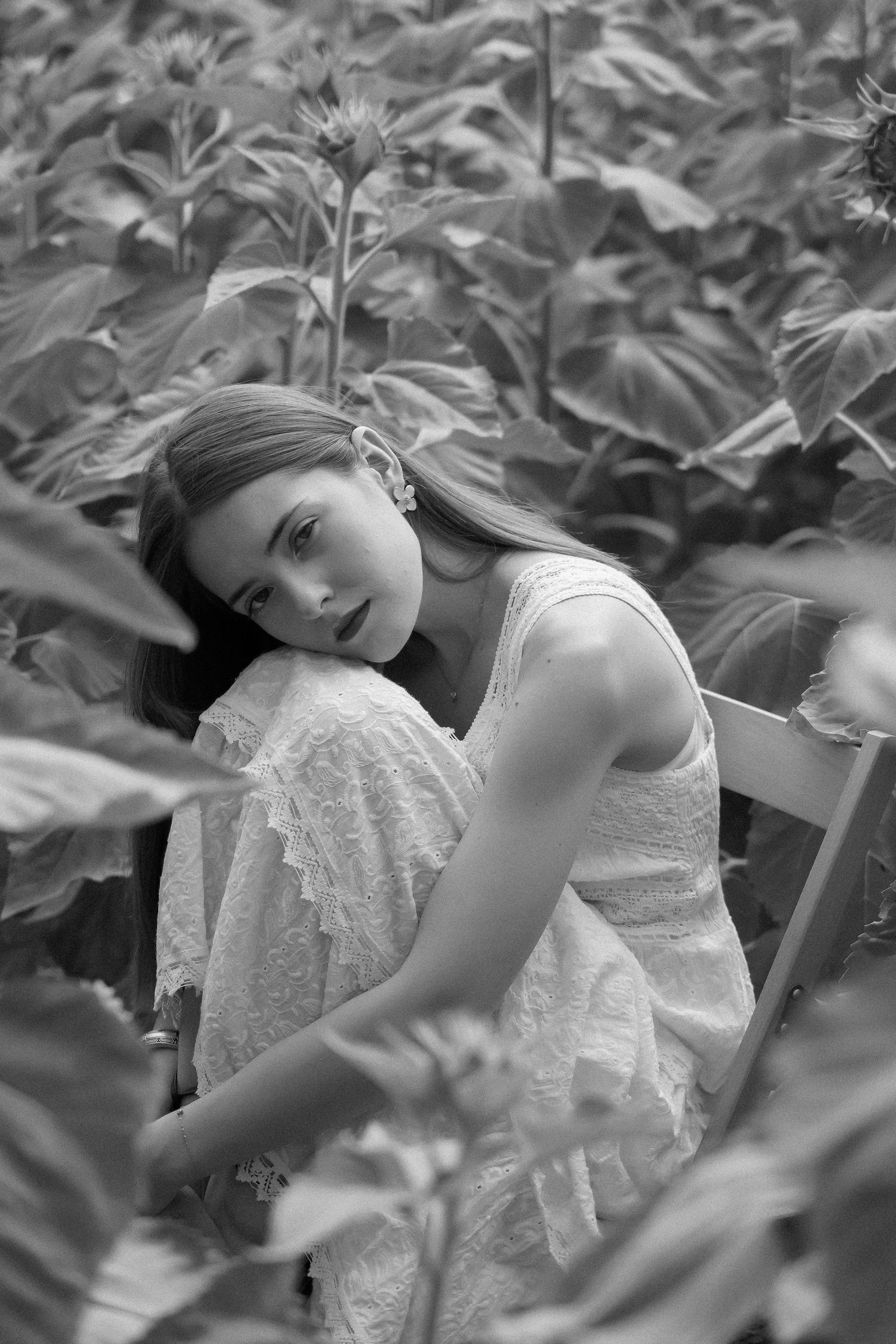 Black and white portrait of a thoughtful woman seated in a sunflower field, evoking elegance and tranquility.