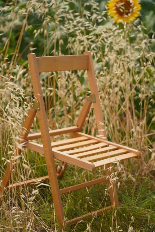 Free A wooden folding chair set in a rural grass field with sunflowers in the background. Stock Photo
