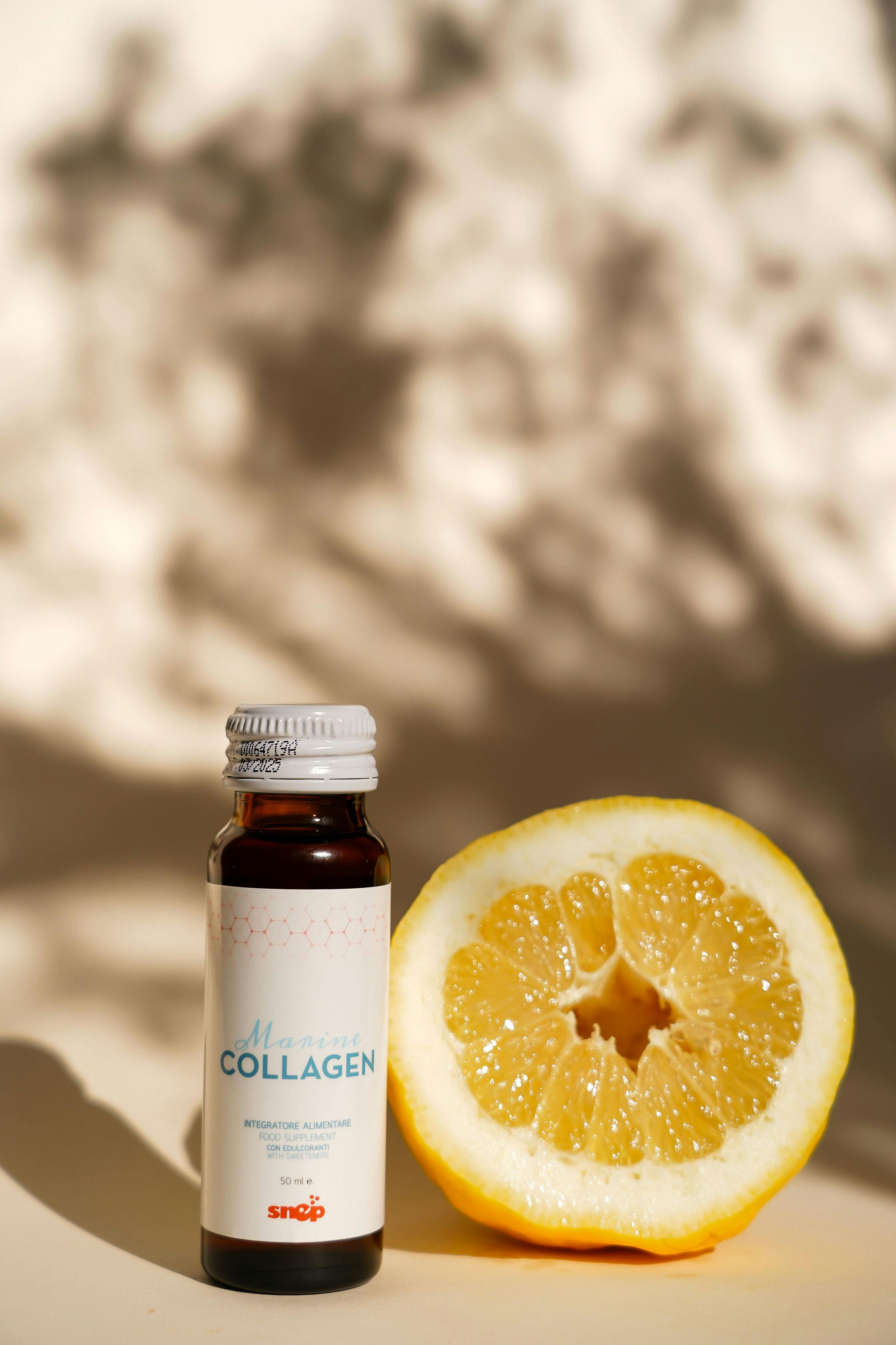 A bottle of collagen supplement next to a sliced citrus fruit in natural lighting, emphasizing health and freshness.
