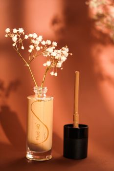Aesthetic still life with a glass bottle, delicate flowers, and makeup in warm light.