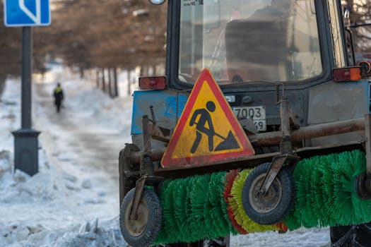 A snow tractor equipped for urban street cleaning clears a snowy path in the city.