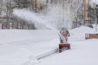 A person operating a snow blower in a winter urban landscape.