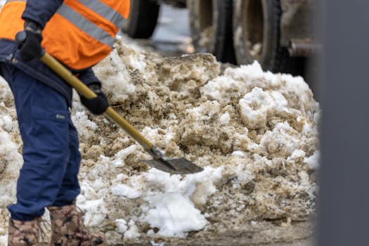 A worker dressed in high visibility clothing shoveling snow during winter maintenance.