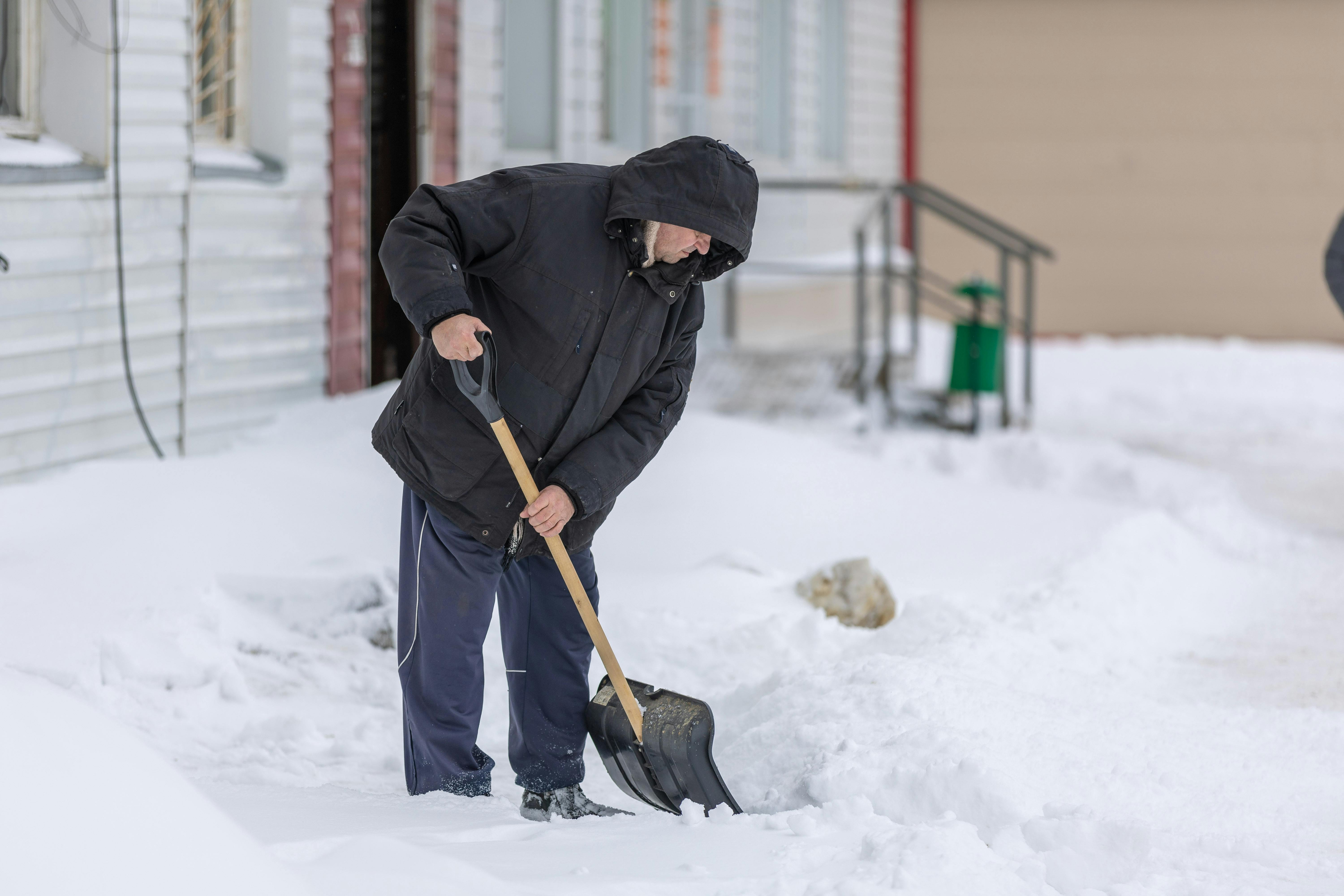 Adult man clearing snow with a shovel during a cold winter day, showcasing winter weather activities.