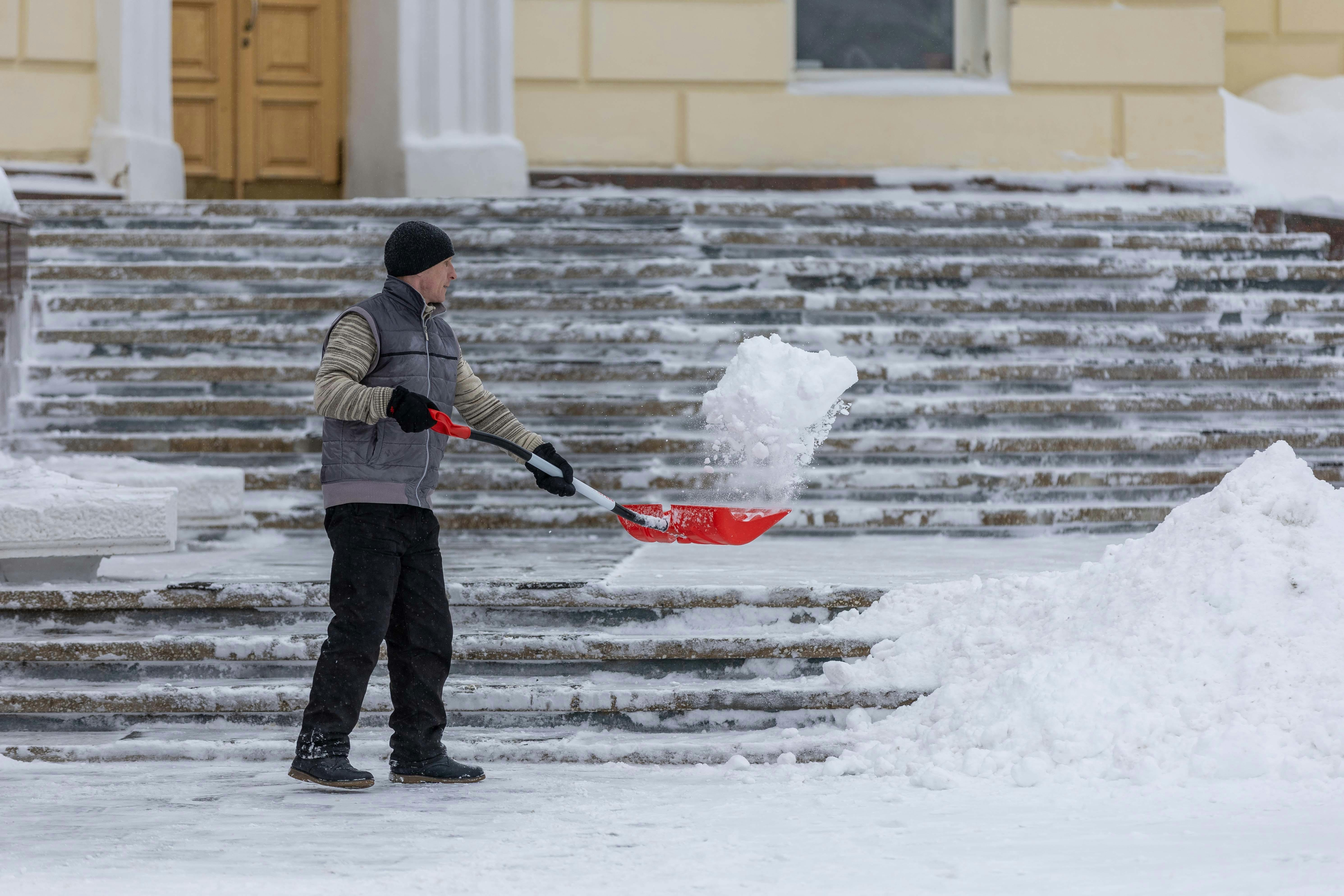Man shoveling snow from steps of building with red shovel.