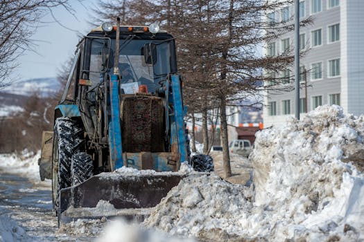 A blue tractor plowing snow in an urban area during winter, ensuring road clearance.