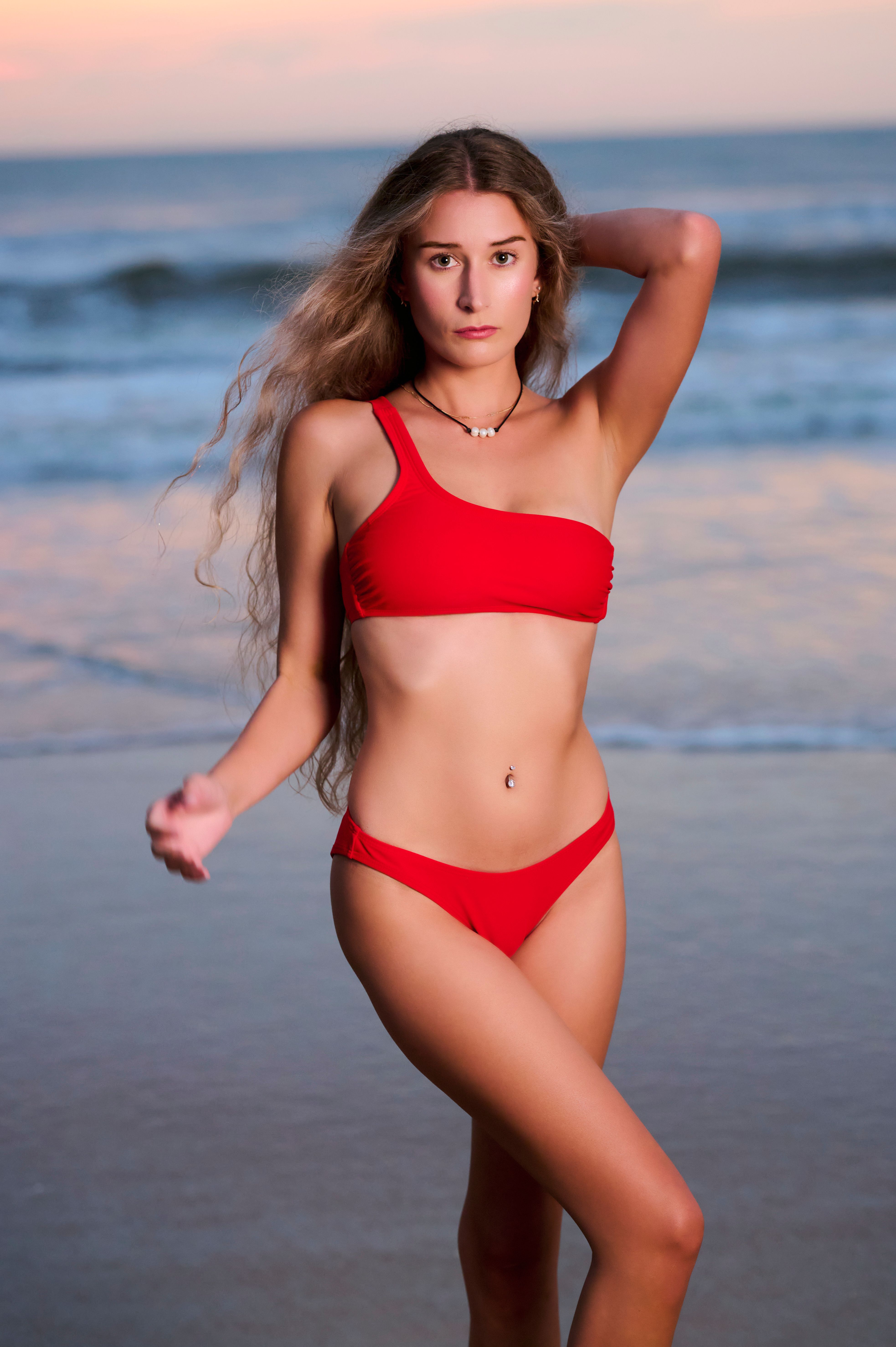 Woman in a red bikini posing on a beach during sunset, showcasing summer fashion.