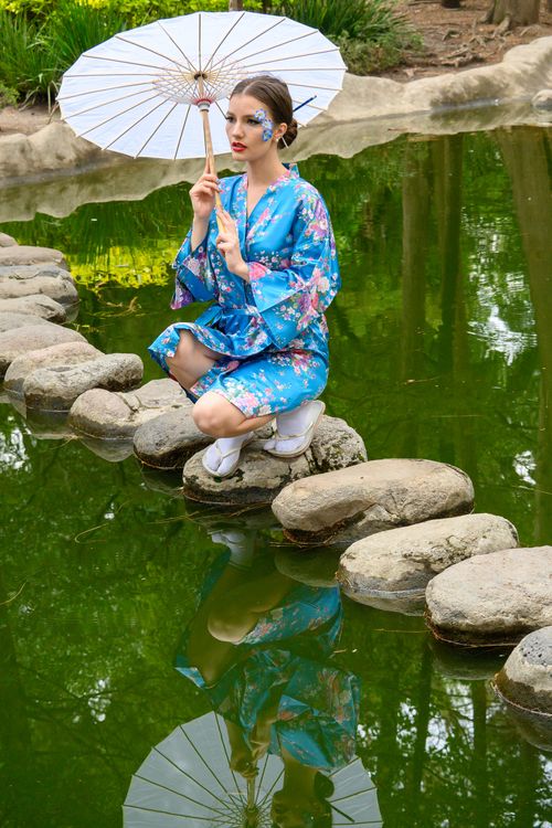 Free A woman in a floral kimono poses with an umbrella near a serene pond, reflecting Japanese culture. Stock Photo