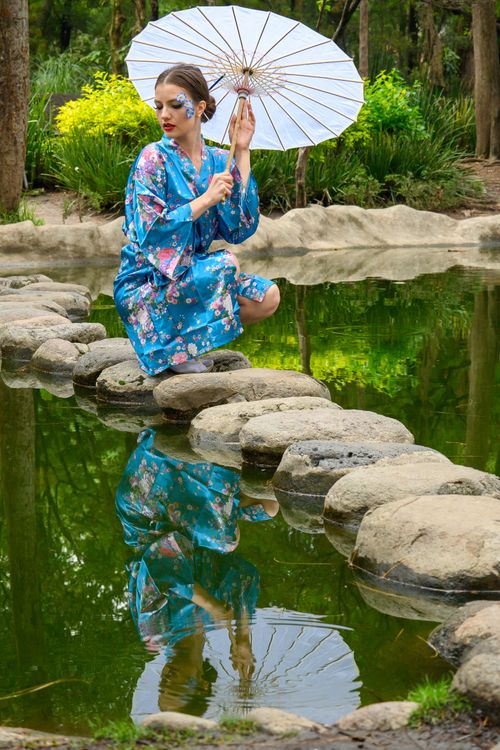 Free A woman in a blue kimono holding an umbrella by a serene garden pond. Stock Photo