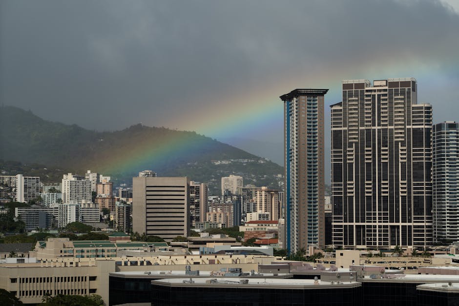 Photo by Donovan Kelly Captivating view of a rainbow arching over the urban skyline of Honolulu, Hawaii, against a stormy sky.
