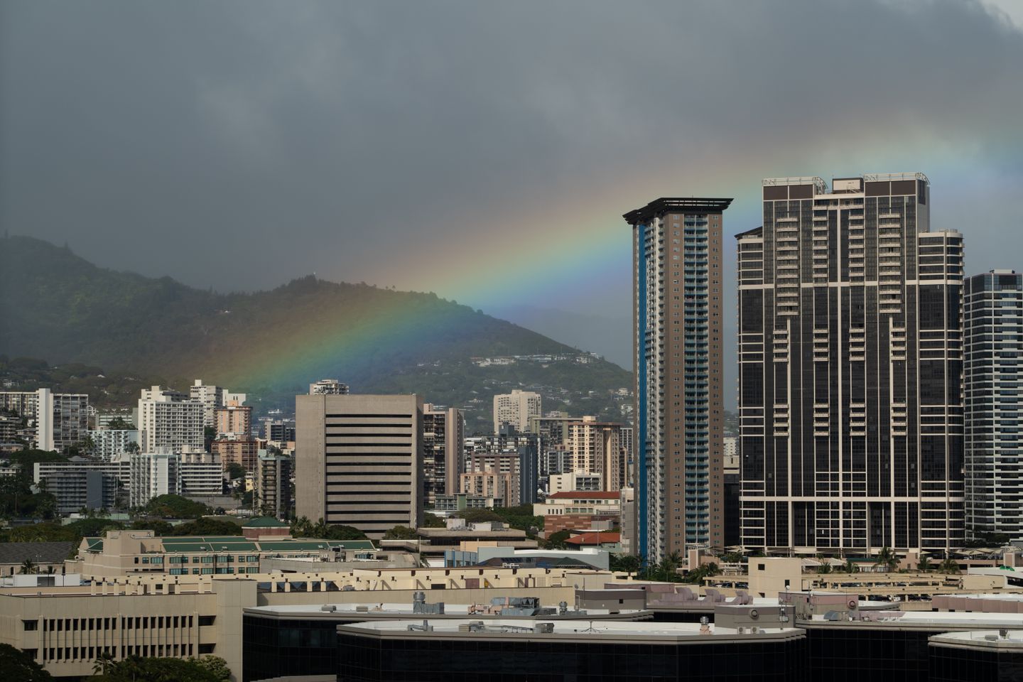 A rainbow arching over the Honolulu skyline under a stormy sky