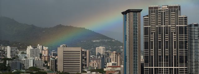Captivating view of a rainbow arching over the urban skyline of Honolulu, Hawaii, against a stormy sky.