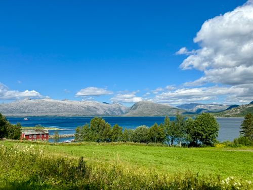 Free Explore a vibrant Nordic countryside with lush greenery, mountains, and a serene lake under a bright blue sky. Stock Photo