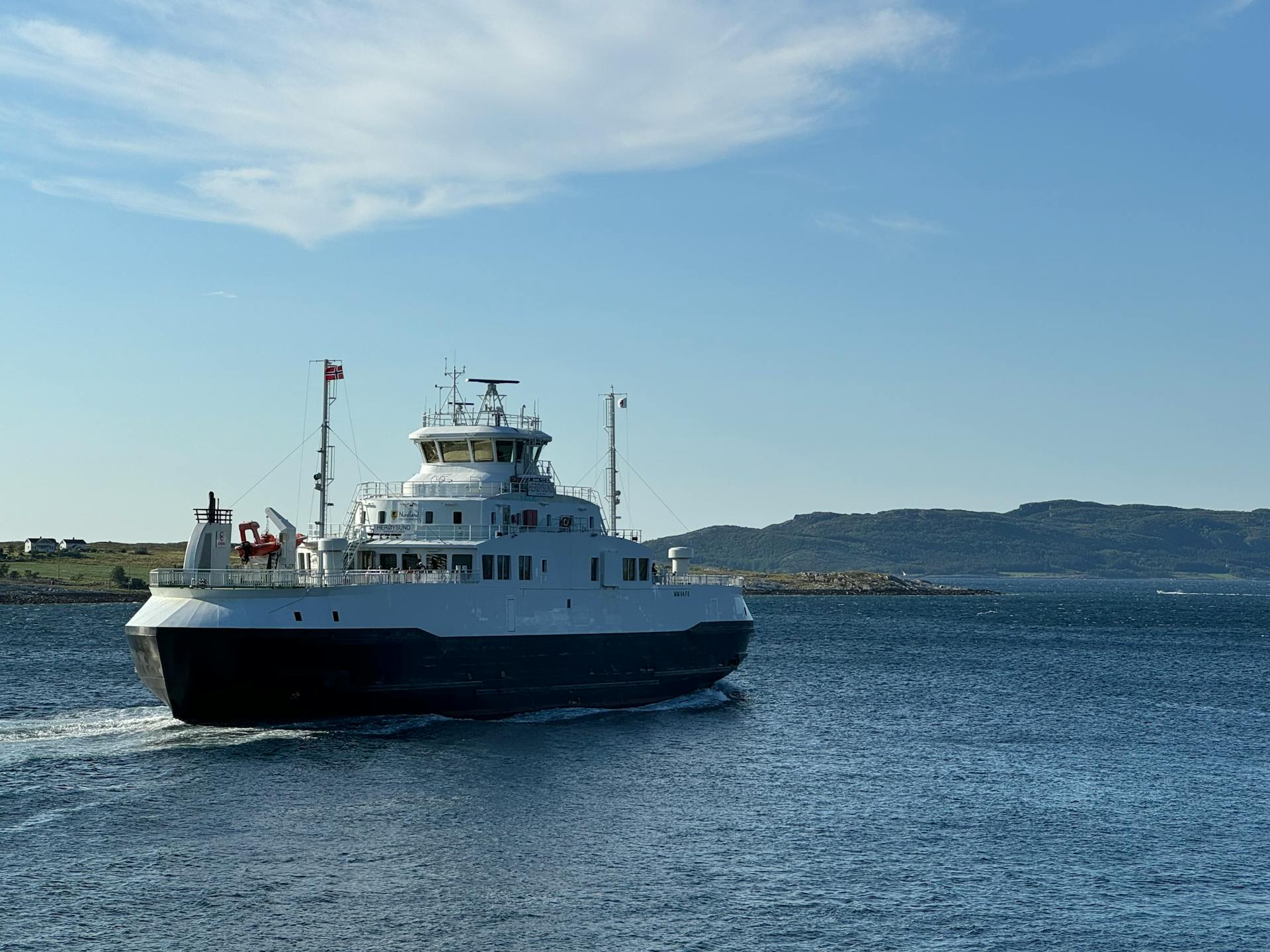 A ferry navigates the calm sea near a picturesque coast under bright blue skies, perfect for travel and transportation imagery.
