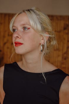 Striking portrait of a young woman with red lips and hoop earrings against a warm wooden background.