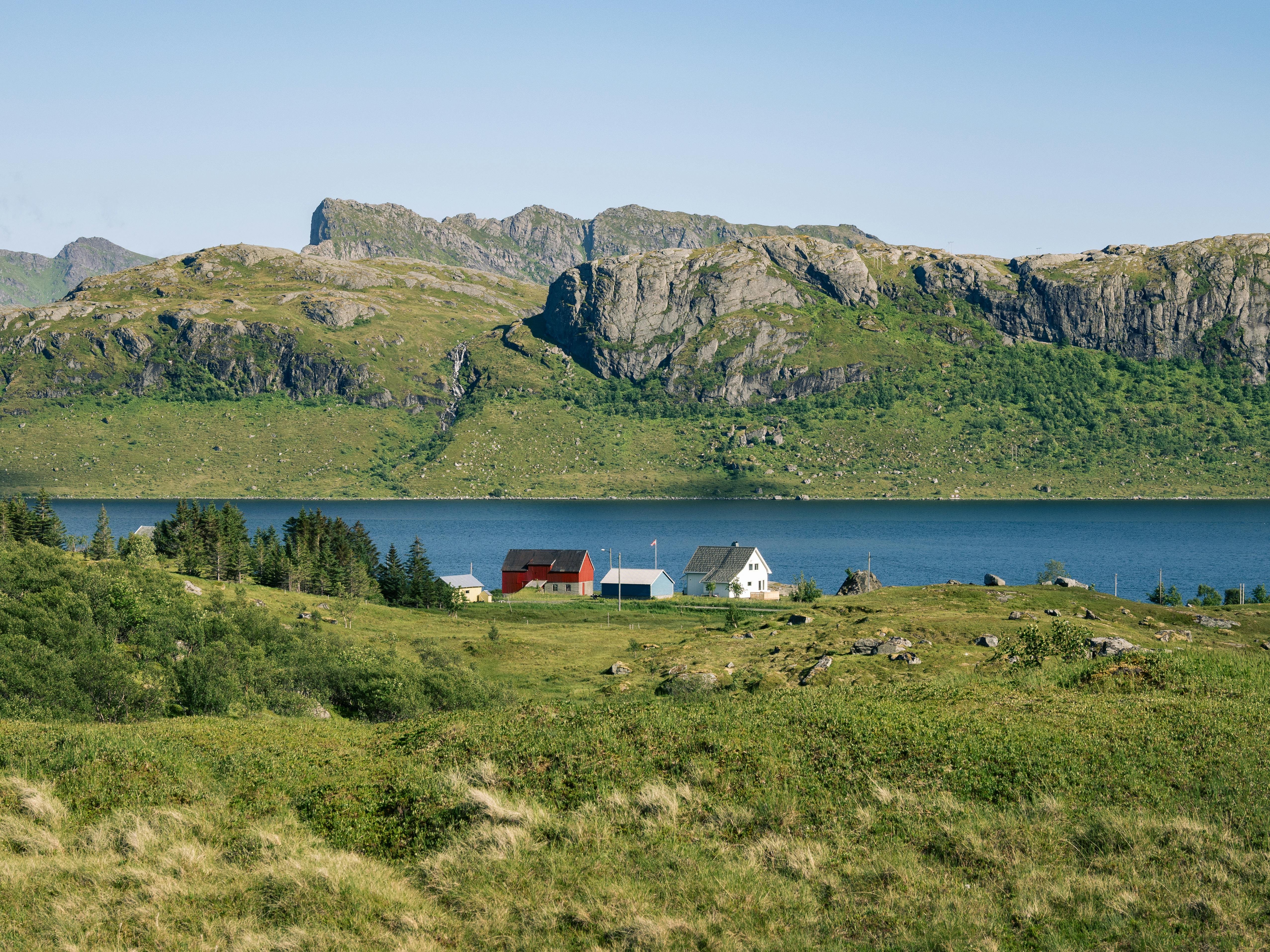 a small house sits on a grassy hillside near a lake