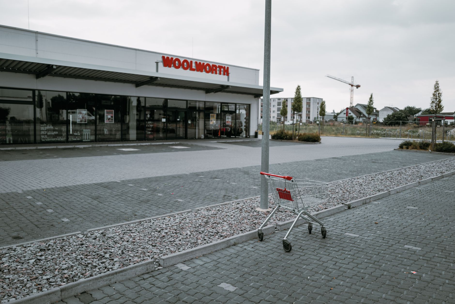 An empty parking lot with an abandoned shopping cart in front of a Woolworth store on a cloudy day.