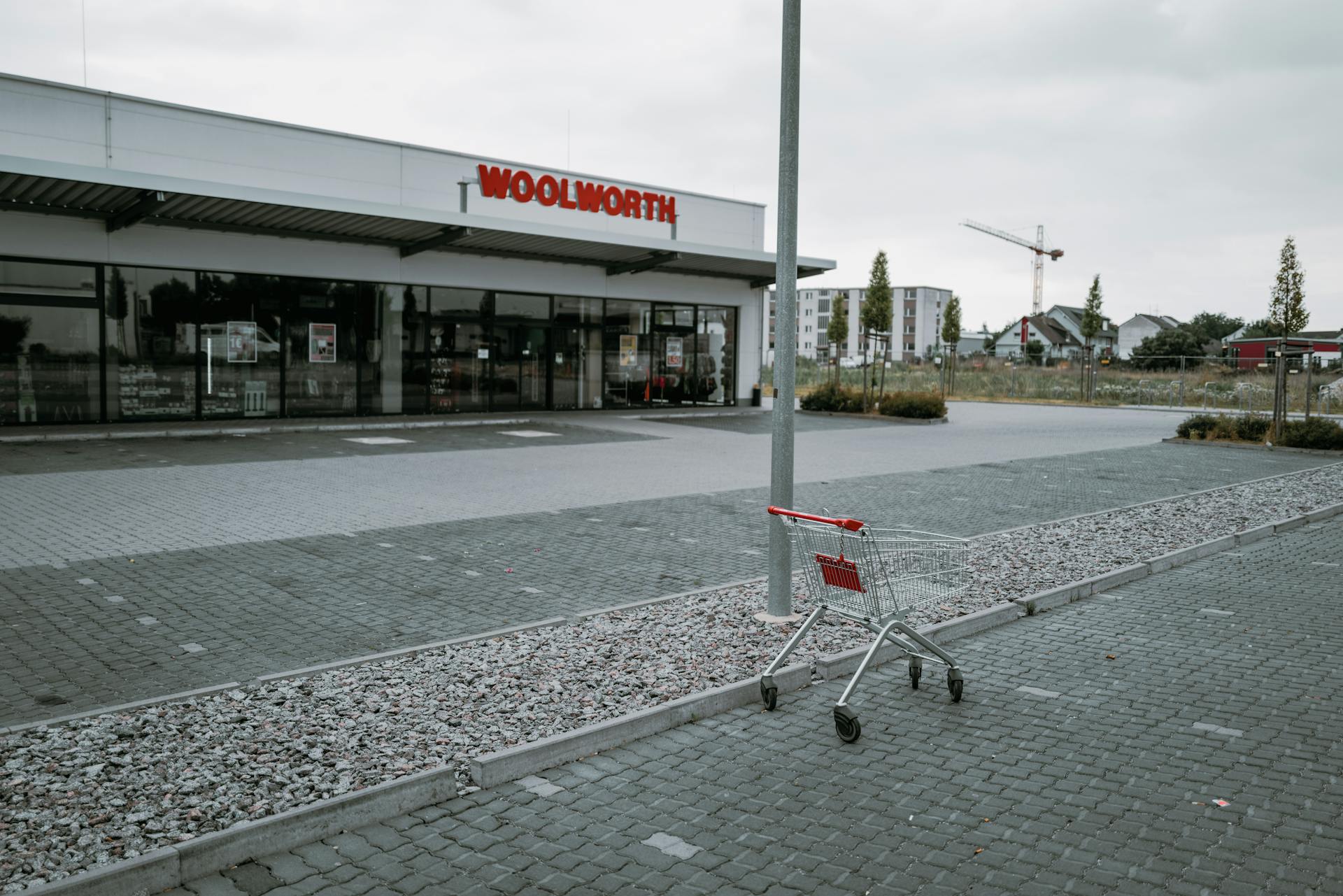 An empty parking lot with an abandoned shopping cart in front of a Woolworth store on a cloudy day.