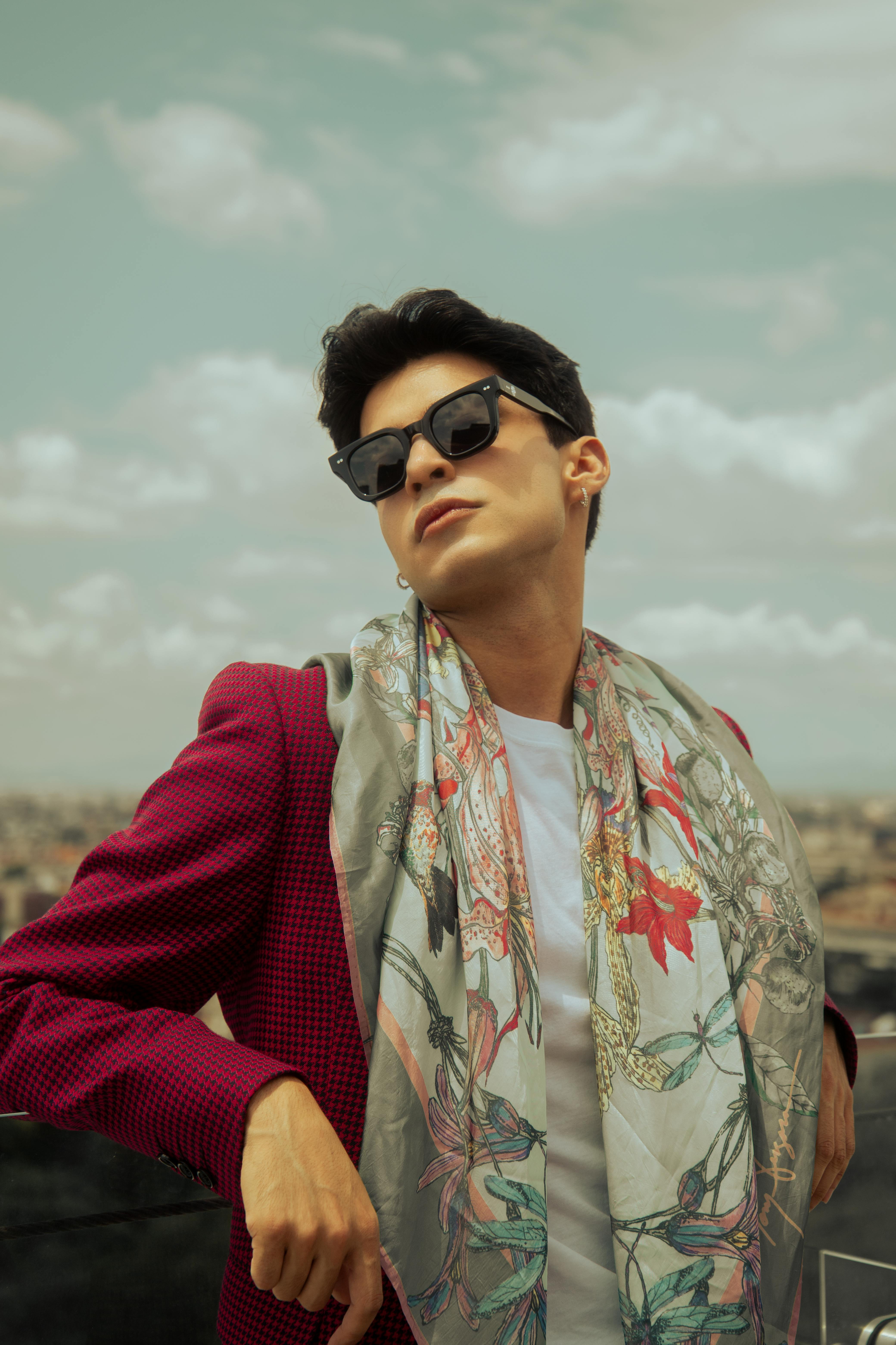 Fashionable man posing on a rooftop in Mexico City, showcasing summer style with sunglasses and a floral scarf.