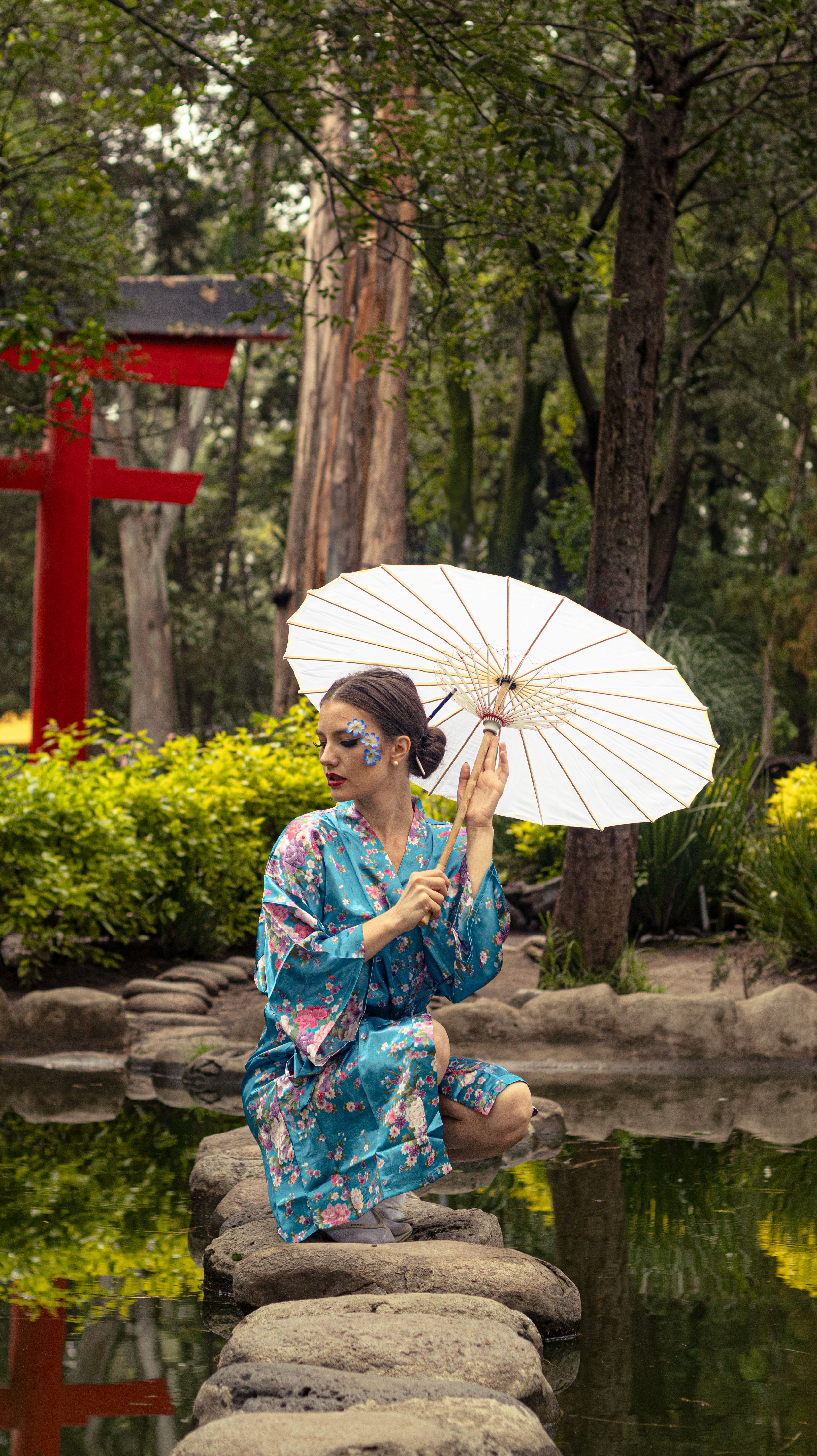 A woman in a kimono with a parasol sits by a serene Japanese garden.