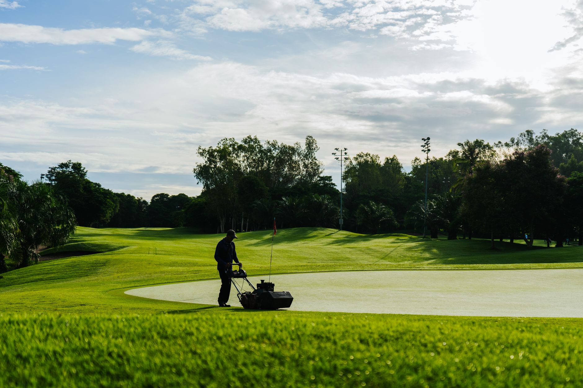 Groundskeeper mowing the green on a golf course during a sunny day, showcasing lush landscapes and maintenance.