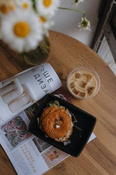A cozy breakfast setup with coffee, flowers, and a magazine on a wooden table.