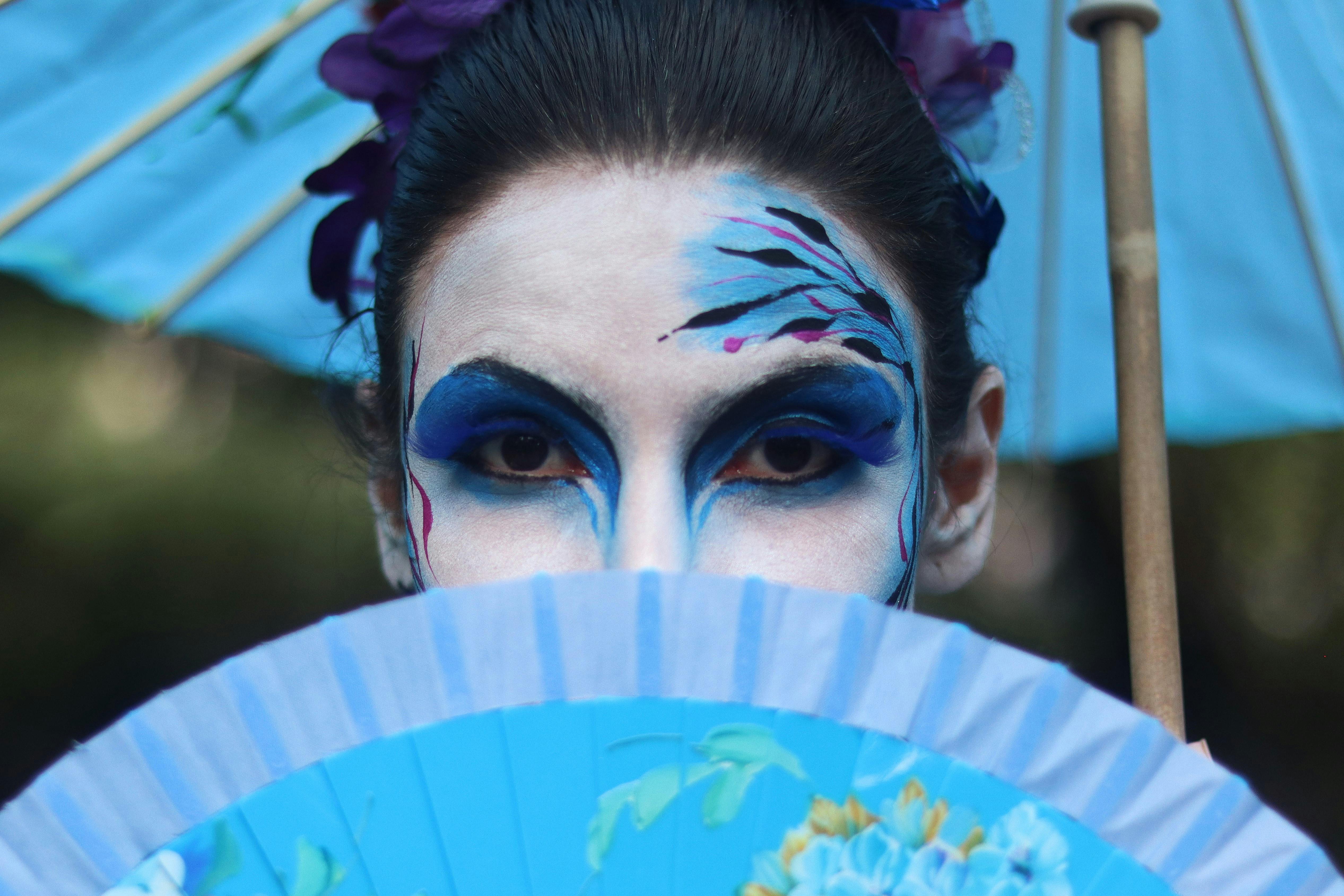 a woman with blue face paint and blue and white fan