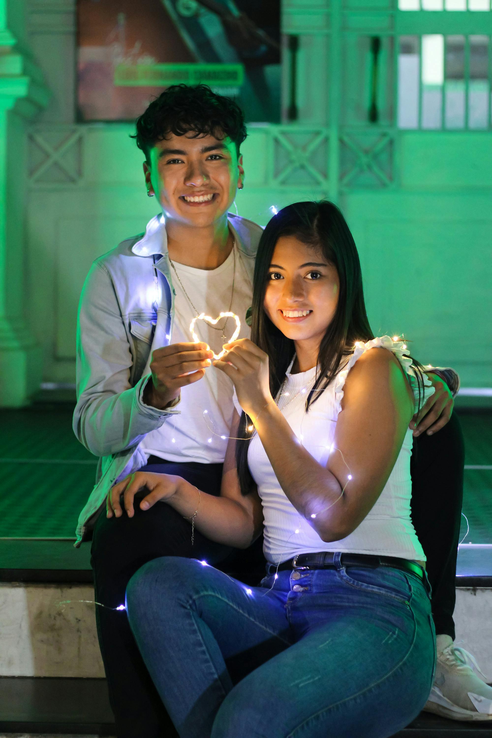 a young couple sitting on a bench holding a lighted heart