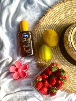 Flat lay of summer essentials: sunscreen, strawberries, lemons, and a straw hat on a blanket.