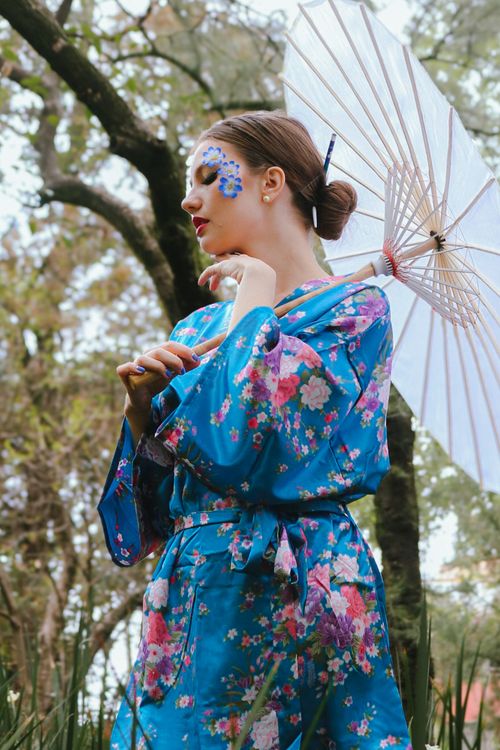 Free A woman wearing a blue floral kimono and holding a parasol in a serene outdoor setting. Stock Photo