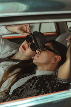 A fashionable couple lounging in a car, wearing sunglasses and enjoying leisure time.