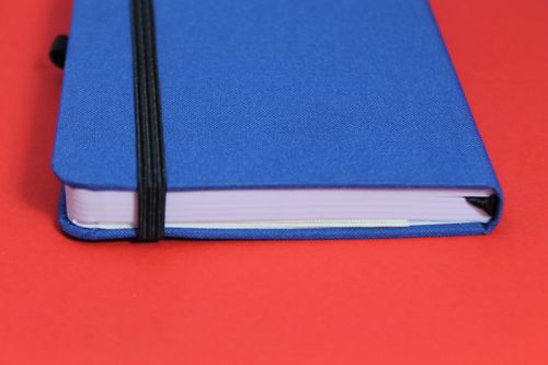 Free A stylish blue journal with a black elastic band resting on a vibrant red surface. Stock Photo