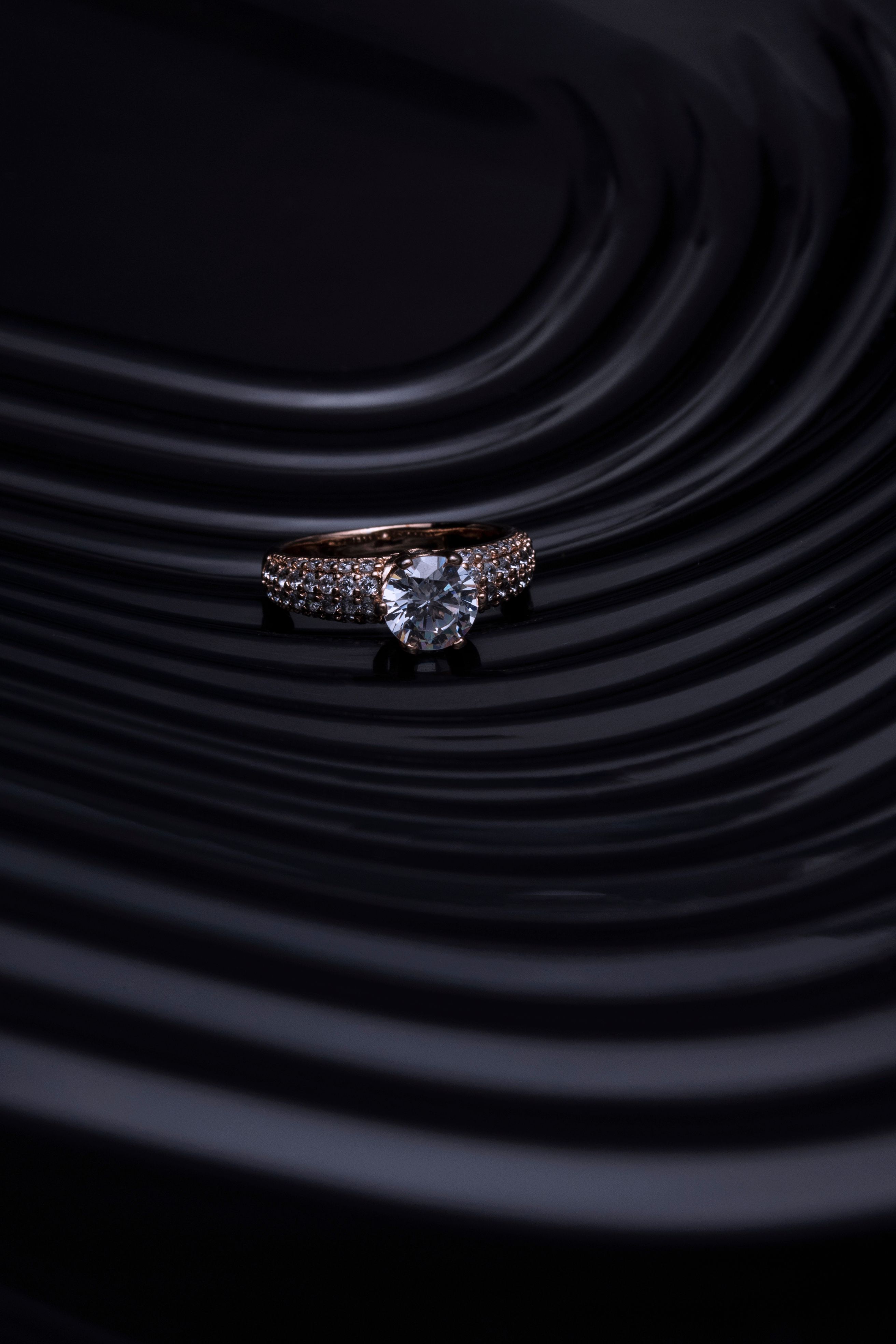 Close-up de um anel de diamante com um fundo escuro e ondulado, criando uma atmosfera luxuosa e elegante.