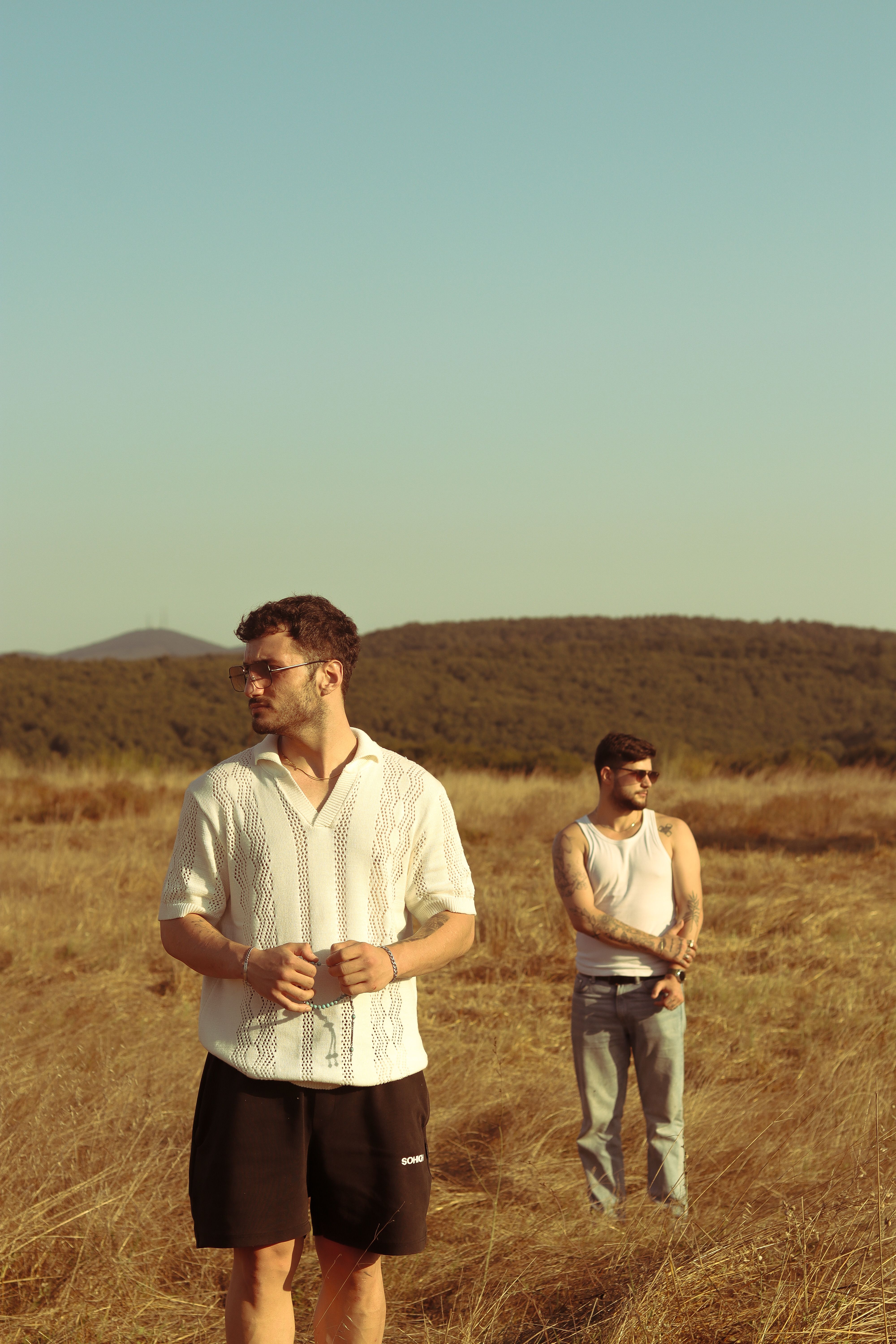 Two men stand in a grassy field under a clear sky, capturing a serene rural scene.