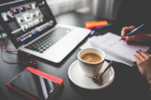 Taza llena de café en el platillo al lado de Macbook y Iphone en el escritorio