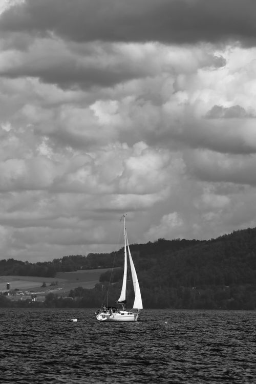 Free A sailboat glides on a lake under a dramatic cloud-filled sky in monochrome. Stock Photo