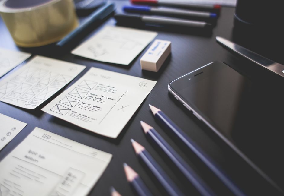 A creative workspace featuring UI design plans, pencils, a smartphone, and other office tools.