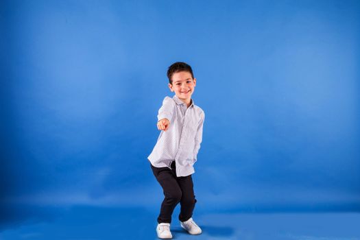 Cheerful young boy in a striped shirt posing playfully in a studio with a blue backdrop.