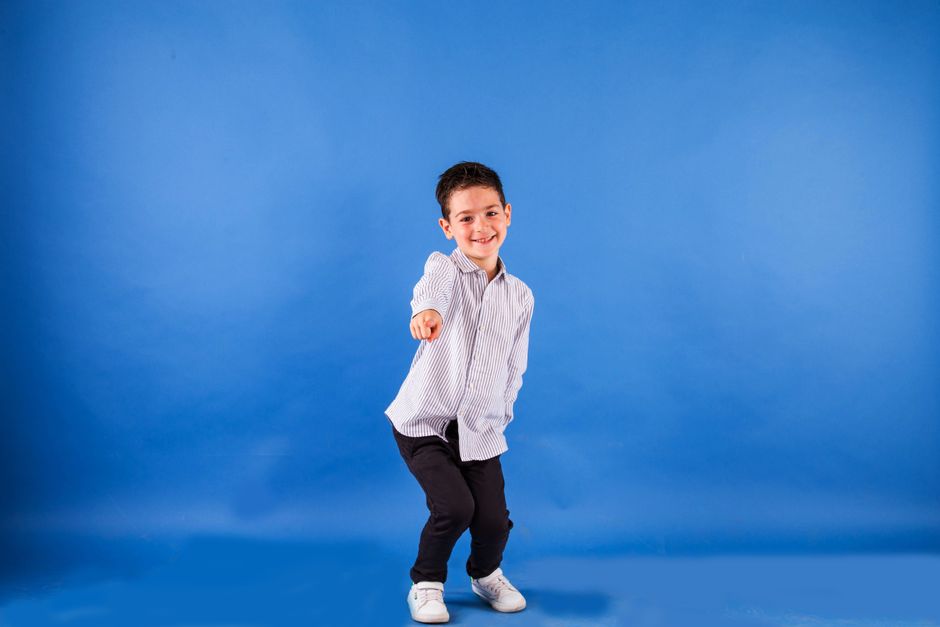 Cheerful young boy in a striped shirt posing playfully in a studio with a blue backdrop.