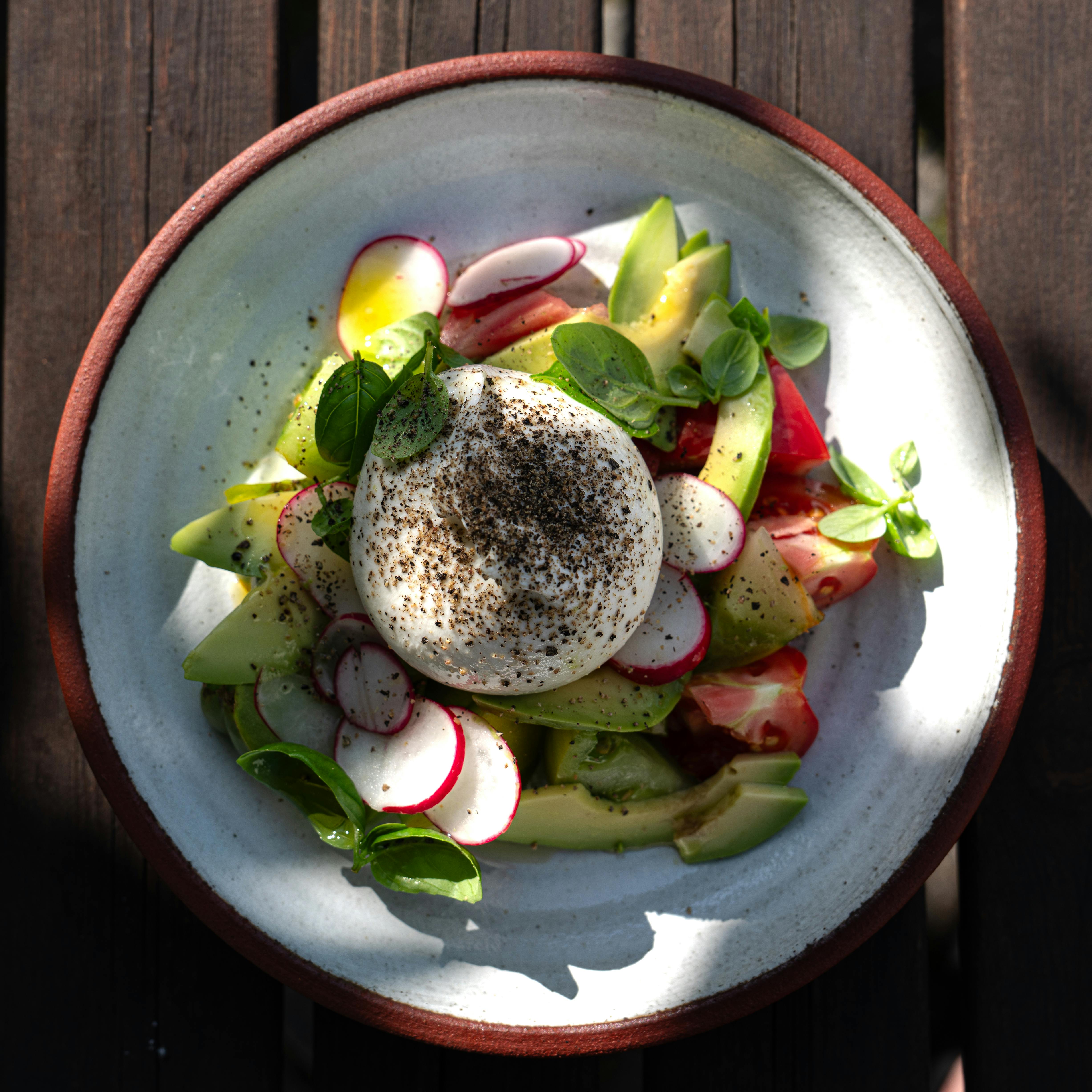 Thomas Svensson - Delicious burrata salad with fresh basil, tomatoes, radishes, and avocado on a rustic wooden table.